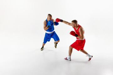 Action shot of two fighters, exchanging blows and testing their endurance in sparring session against white studio background. Concept of professional sport, healthy lifestyle, competition. Ad