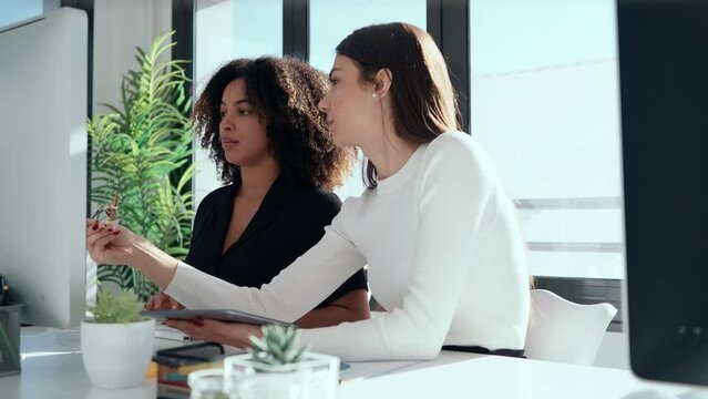 Video of two attractive business women talking and working with computer and digital tablet in coworking place