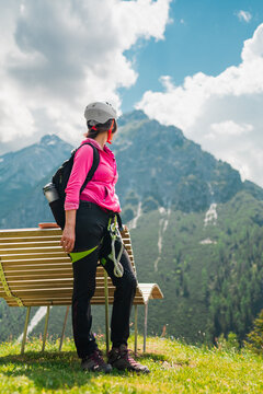 Woman Climber with Climbing Equipment Standing on a Bench Looking into the Distence of a Mountain Landscape