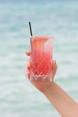 Woman holding a glass full of red refreshing drink against blue sea, Cold-Brew Iced Sweet Hibiscus Tea,  summer refreshing drink, detox, diet and healthy lifestyle concept.	