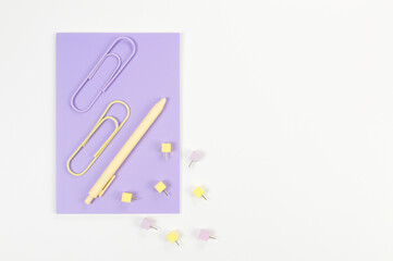 Top view of purple notebook on white background. Paperclips, pen and pins. School, office wallpaper. Flat lay, copy space.