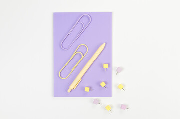 Top view of purple notebook on white background. Paperclips, pen and pins. School, office wallpaper. Flat lay, copy space.