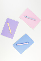 Top view of pink, purple and blue notebooks on white background. Pink, yellow and blue pens, school, office wallpaper. Flat lay, copy space.