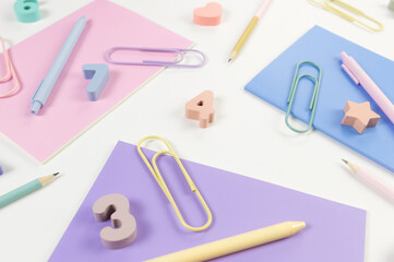 Top view of pink, purple and blue notebooks on white background. Colorful pens, pencils, paperclips, numbers, shapes and pins. School, office wallpaper. Flat lay, copy space.