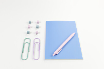 Top view of blue notebook on white background. Paperclips, pen and pins. School, office wallpaper. Flat lay, copy space.