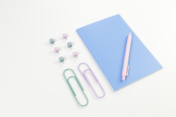 Top view of blue notebook on white background. Paperclips, pen and pins. School, office wallpaper. Flat lay, copy space.