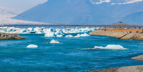 Aerial view of a suspension bridge spanning a river with floating ice floes, surrounded by...