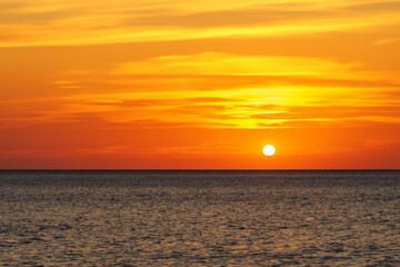 Obraz premium Sunset over the sea and sky. Sunrise ocean beach concept. Sunset over the sea with oranges and the sun in nature. Sunset with oranges and sun against a blue sky in lifestyle nature.