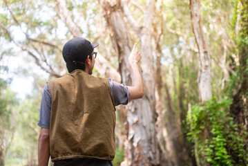 Happy asian man pointing finger in mangrove forests. He admires lush foliage, serene ambiance in tropical botanical garden. Traveler enjoys eco-tourism, nature walks.