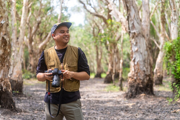 Happy asian man explores mangrove forests with camera. He admires lush foliage, serene ambiance in tropical botanical garden. Traveler enjoys eco-tourism, nature walks.