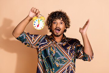 Photo portrait of attractive young man hold clock amazed dressed stylish print clothes isolated on beige color background