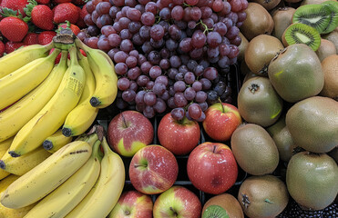 A colorful display of fresh fruits including strawberries, bananas, grapes and kiwi arranged in rows on the counter. Created with Ai