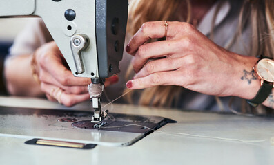 Woman, hands and fashion designer with thread on sewing maching for clothing production at workshop. Closeup of female person, dressmaker or seamstress working with string or fabric for knitting