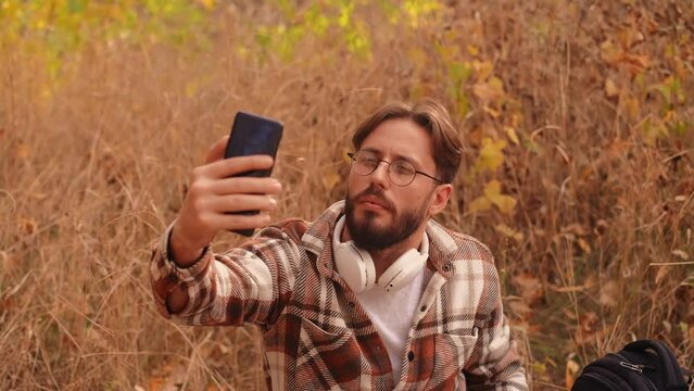 Young male blogger relaxing in nature away from the city, creating vlogs about hiking using his smartphone.