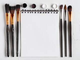Art supplies including various paintbrushes and a blank notebook on a white background, ideal for creative projects and planning.