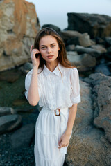 Serene young woman in flowing white dress listens intently on rocky beach