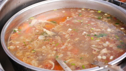 A pot of steaming hot soup ready with a lot of vegetables, herbs and spices for delicious and healthy soup.