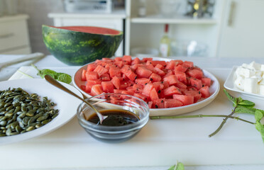 Making a healthy summer salad with watermelon, feta cheese, balsamic vinegar and pumpkin seeds
