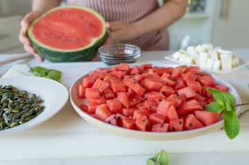 Homemade summer food. Woman preparing a fresh salad with watermelon, feta cheese and pumpkin seeds