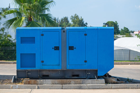 Blue mobile diesel generator for emergency electric power. Street dog protected from the sun next to the generator.