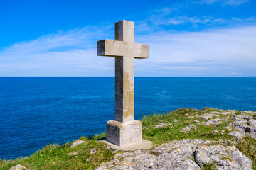 A Christian cross stands tall on a hill, with the vast expanse of the ocean in the background. The scene captures the cross as it overlooks the sea, symbolizing faith and spirituality.