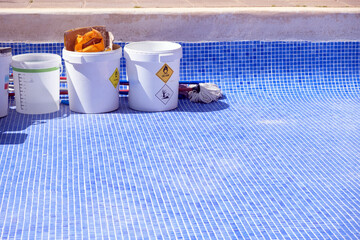 Trash cans lined up beside an empty pool during repair and sealing work.