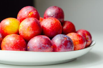 A white plate with a bunch of red plums on it