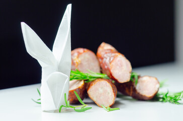 A pile of sausages with a white napkin and a paper rabbit on top