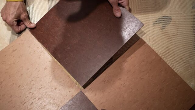 Closeup of hands putting a vinyl composition tile, VCT into place on a kitchen floor in a home renovation project.