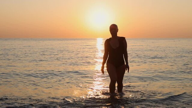 beautiful women with alopecia on beach against sea drag a chair.balt girl in shirt in water, sunrise or sunset time.sun reflection on waves.female in swimsuit.