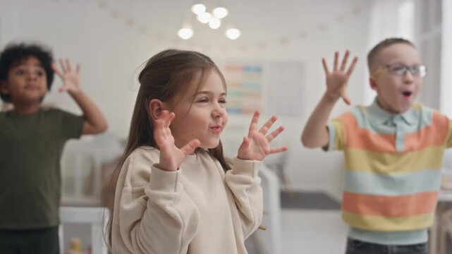 Medium shot of multiethnic preschool children making dancing movements, smiling and grimacing while doing morning exercise at kindergarten, repeating after offscreen educator