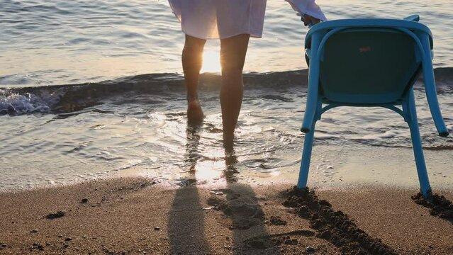 beautiful women with alopecia on beach against sea drag a chair.balt girl in shirt in water, sunrise or sunset time.sun reflection on waves.female in swimsuit.