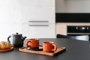 Selective focus on bamboo board with cups, teapot and plate with bakery on table