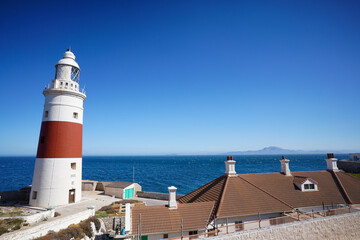 Europa Point Lighthouse facing the strait of Gibraltar on top of sea cliffs with the mountains of Morocco in the distance.