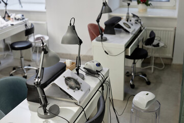Shot of manicurist workplace equipped with nail tech desks with dust collectors and table lamps. White clean interior of empty beauty salon