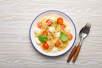 Delicious spaghetti with tomatoes and mozzarella cheese served on white wooden table with cutlery aside, top view