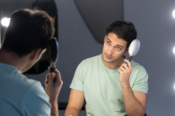 In front of the mirror, a man meticulously grooms himself, his reflection capturing the focused...