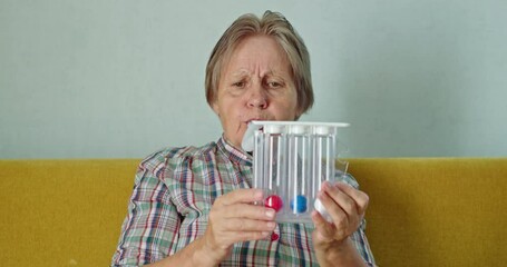 An elderly woman blows into a special device - spirometer to train her lungs and test lung capacity