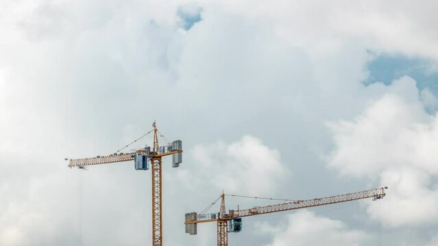 Big construction site including several cranes working and moving on a building complex, with cloudy sky timelapse. Massive clouds passing by