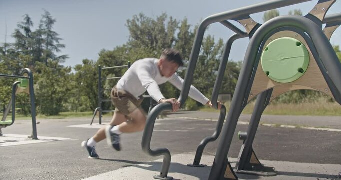 A man exercises on parallel bars in the park, demonstrating outdoor fitness and upper body strength training on a sunny day, showcasing his dedication to a healthy lifestyle.