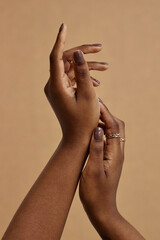 Vertical close up on elegant hands with nude manicure of African American woman. Monochrome nail design in dark brown shades against beige background