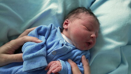 Newborn baby in a blue onesie resting peacefully on a soft blanket, highlighting the tranquility...