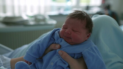 Sleepy newborn baby in a blue onesie, being held gently, capturing the peacefulness and warmth of...