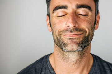Obraz premium A man with a relaxed smile and closed eyes, completely isolated from the environment, set against a plain white background