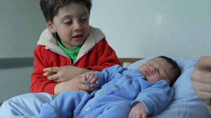 Young sibling holding hands with sleeping newborn baby, representing family bonding, love, and...