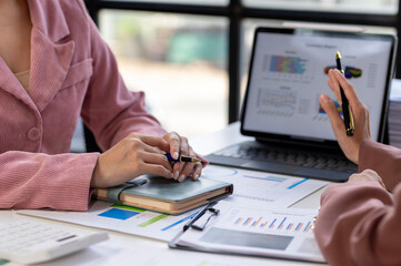 Two women are sitting at a table with a laptop and a notebook