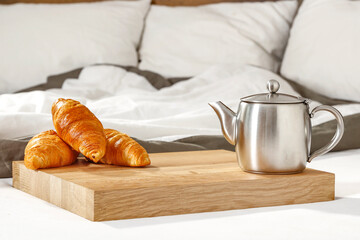 Croissant and drink. Breakfast served in bed on a wooden tray. Blurry background of the bed and bedding.