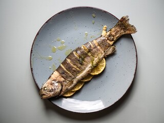 A whole roasted salmon on a plate stuffed with lemon slices