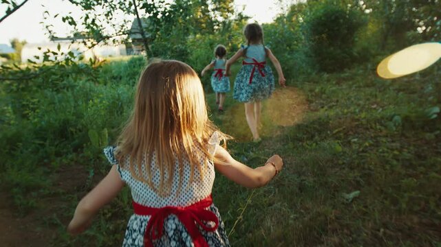 Three girls wearing the same dress run in the summer garden