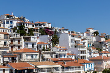 Skiathos, Greece A picturesque marina featuring boats docked by a tranquil coastal town, set against rolling hills under clear blue skies. Ideal for travel and tourism themes.